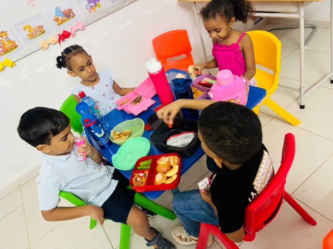 Quatre enfants partagent leur goûter autour d'une table dans une classe colorée